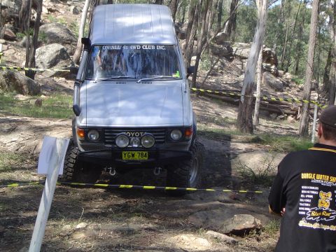 1982 Ford Bronco - Toyota Land Cruiser FJ60 navigating a challenging off-road course with trees and rocks.