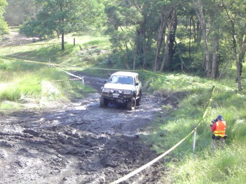 1982 Ford Bronco - A white SUV tackles a challenging muddy course during an off-road event.