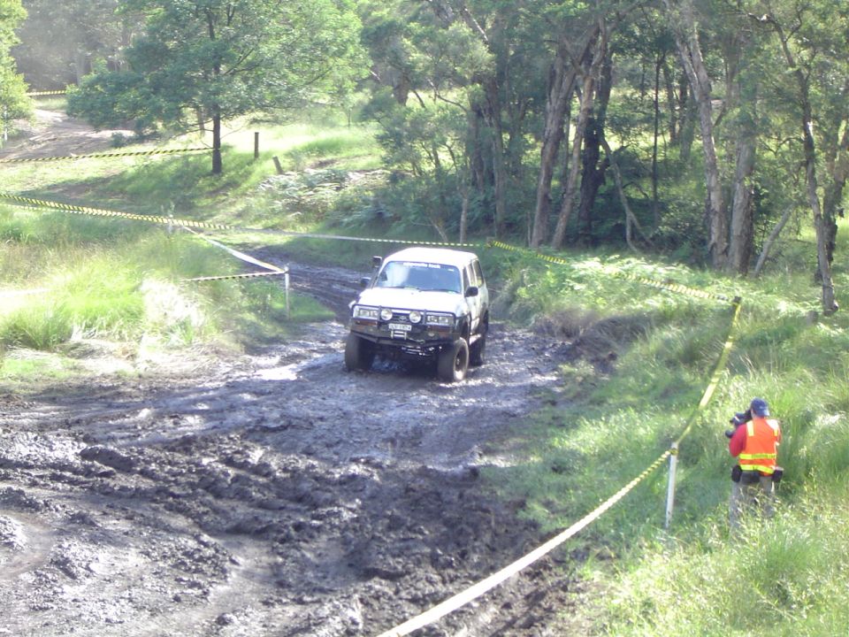 White SUV with off-road tires and a bull bar navigating a muddy track