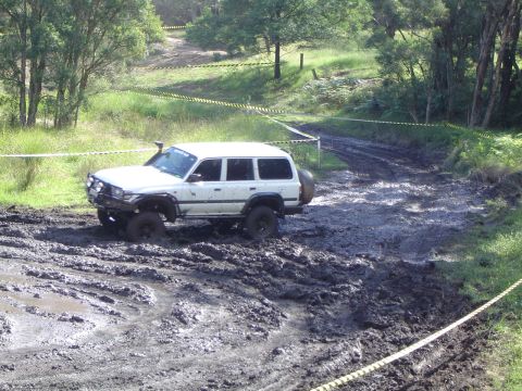1982 Ford Bronco - This white off-road SUV is navigating a challenging muddy track, demonstrating its off-road capabilities.