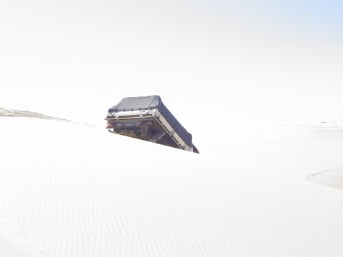 1982 Ford Bronco - A truck with a covered bed is partially buried in sand dunes, its rear end visible against a bright sky.