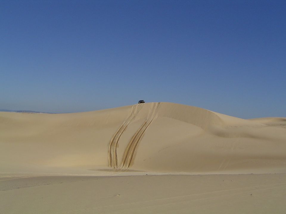 SUV on top of sand dune with tire tracks below