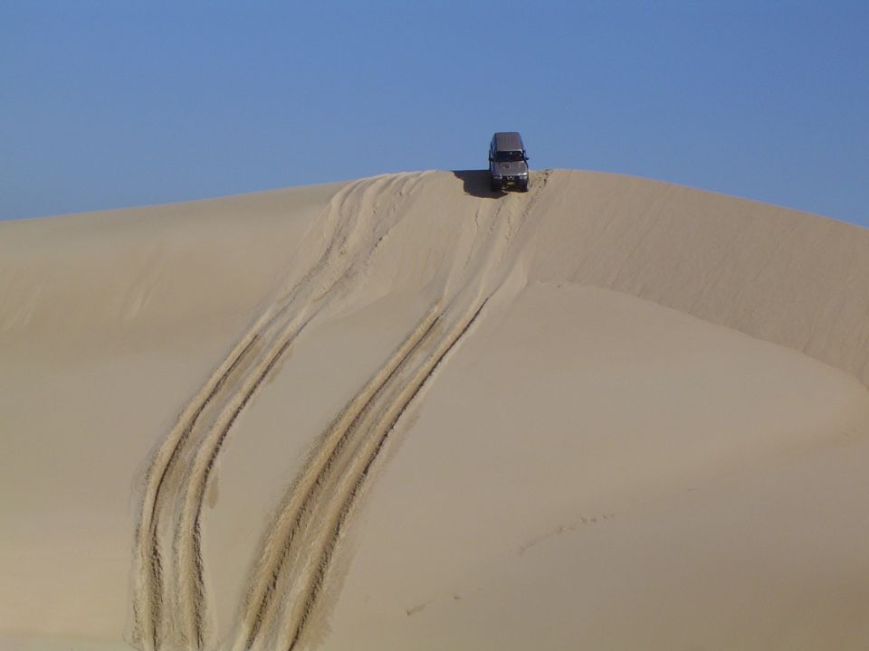 Gray SUV driving up a sand dune, leaving tire tracks