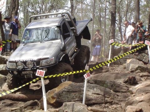 1982 Ford Bronco - A modified Nissan Patrol tackles a challenging off-road course with spectators watching.