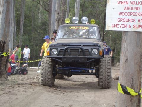 1982 Ford Bronco - A heavily modified off-road vehicle with oversized tires navigates a dirt track.