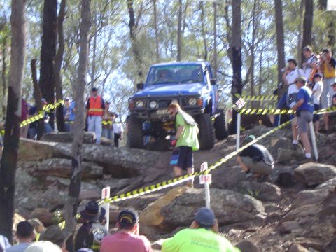 1982 Ford Bronco - A blue SUV navigates a challenging rocky terrain during an off-road event, with onlookers observing the action.