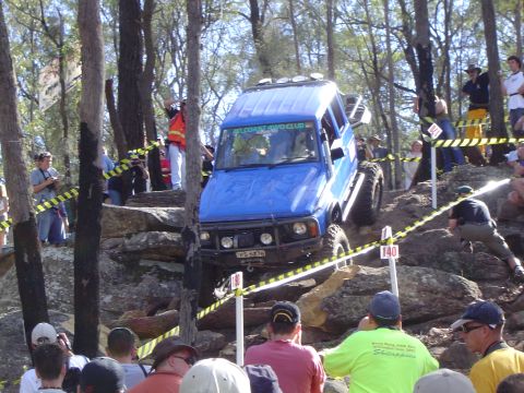 1982 Ford Bronco - A blue off-road SUV tackles a challenging course with spectators observing the action.