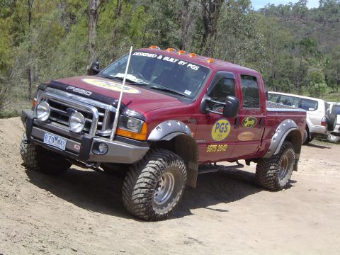 1982 Ford Bronco - Modified Ford F-250 pickup truck with off-road tires and accessories parked on a dirt track.