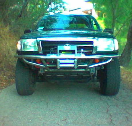 1995 Ford Bronco - A truck with a custom bumper and large tires is parked on a paved surface surrounded by trees.