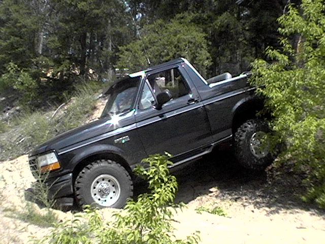 Black Ford Bronco with lifted suspension and off-road tires driving on a dirt hill