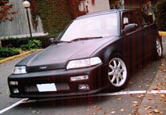 1995 Ford F-150 - This black hatchback is parked on a street with fallen leaves around it.