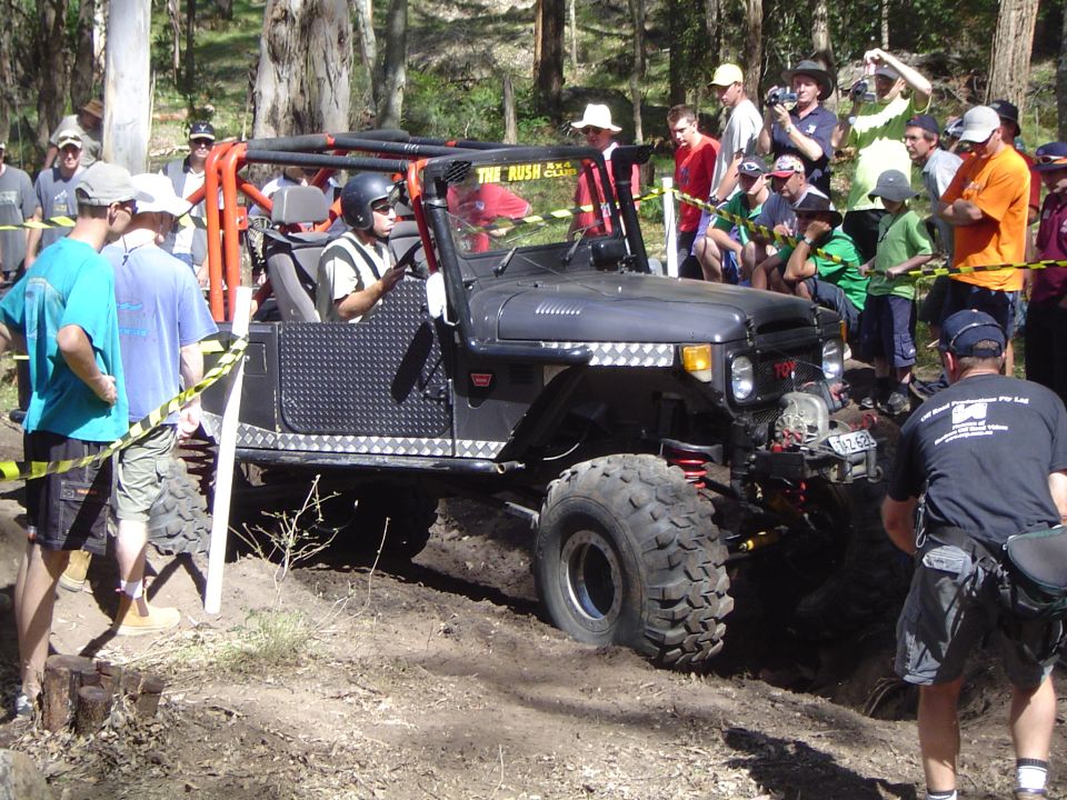 Dark grey off-road vehicle with roll cage, large tires, and diamond plate doors, stuck in dirt