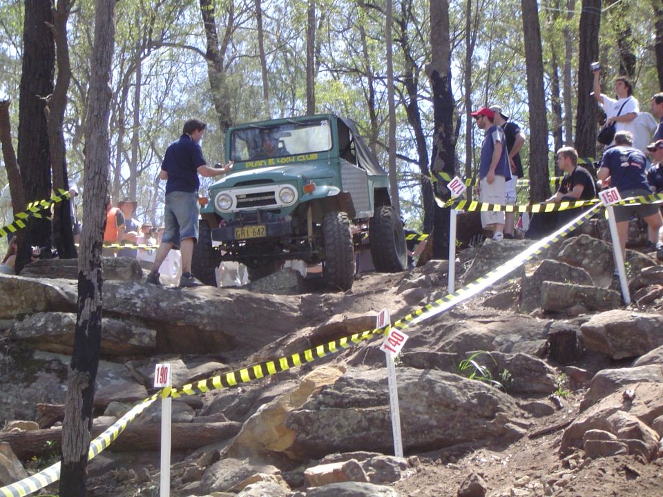 Green Toyota Land Cruiser FJ40 with a soft top, navigating a rocky obstacle course