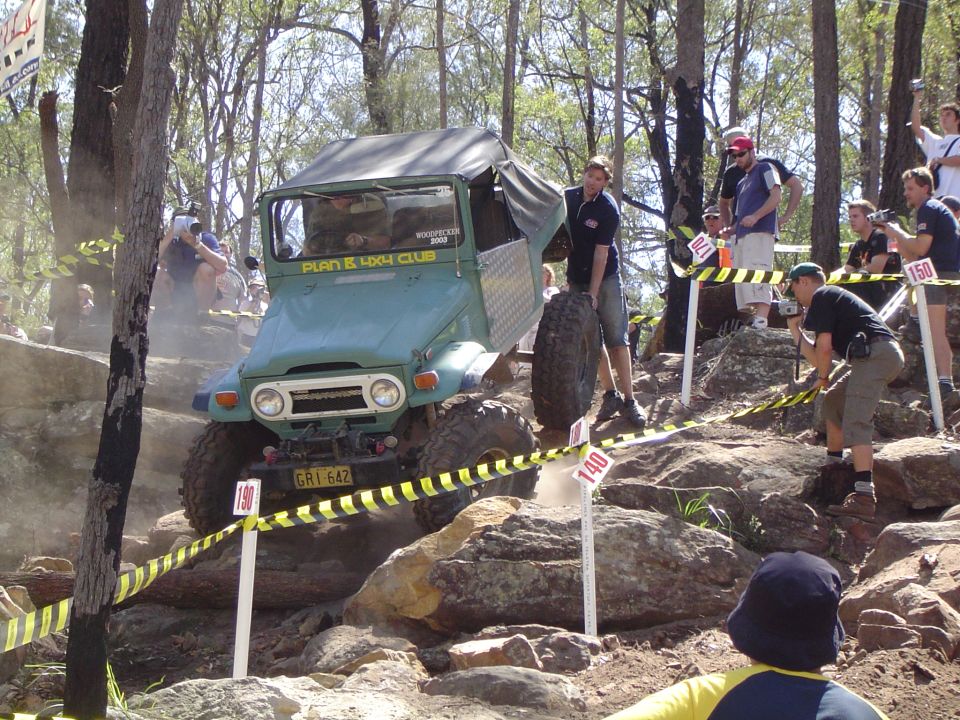 Green Toyota Land Cruiser FJ40 climbing a rocky hill with spectators watching. License plate GR1 642