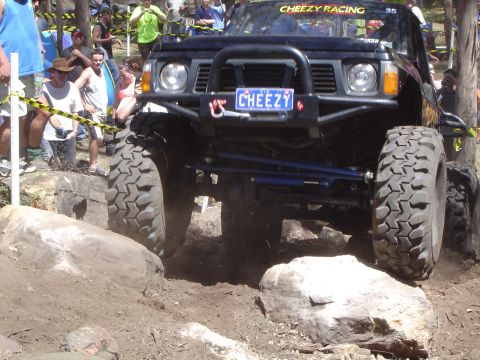 1982 Ford Bronco - An off-road vehicle tackles a rocky course, with spectators watching in the background.