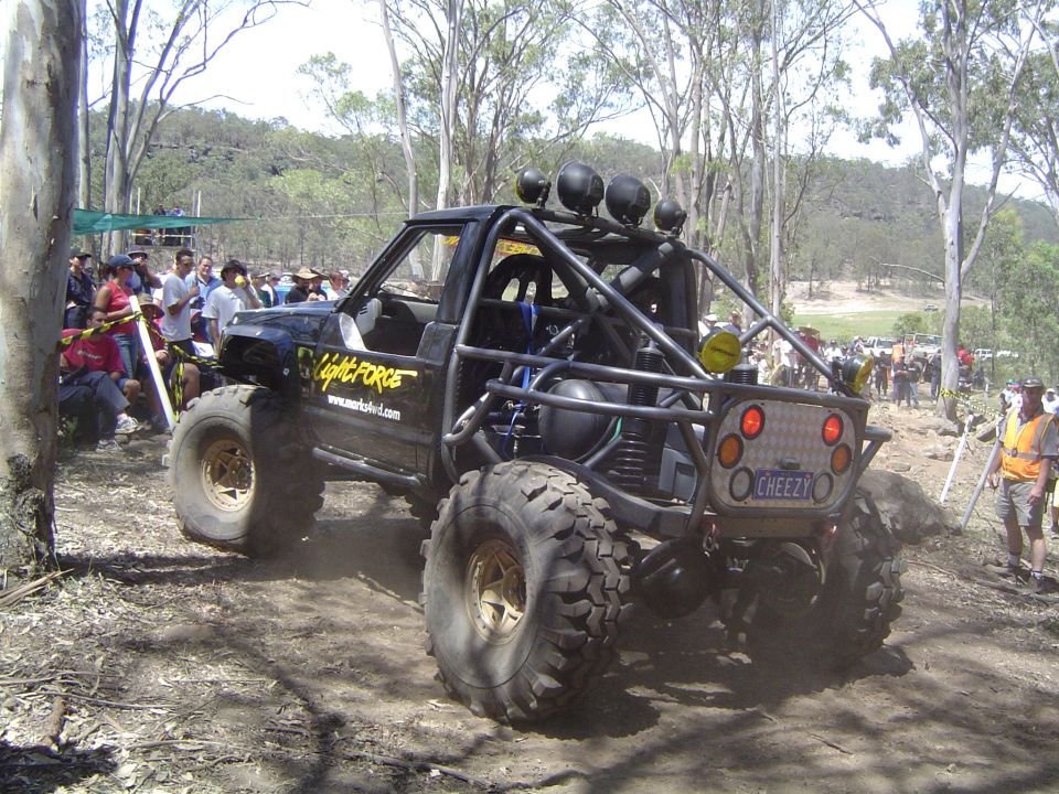 Modified off-road buggy with roll cage and large tires, rear view. License plate reads 'CHEEZY'
