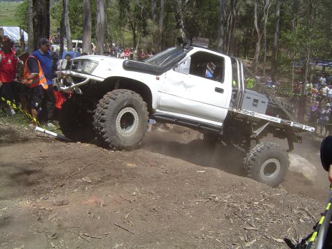 1982 Ford Bronco - Modified white pickup truck navigates a challenging off-road course with spectators watching.