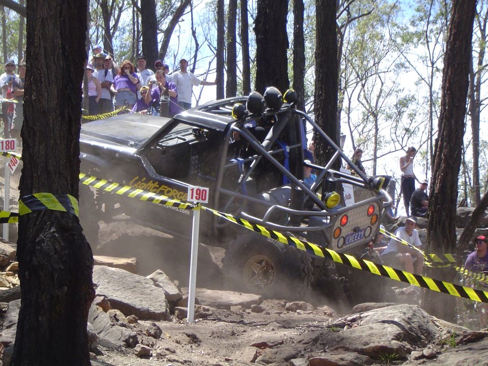 Off-road buggy with roll cage climbing rocks, spectators watching. 'Light Force' visible on side