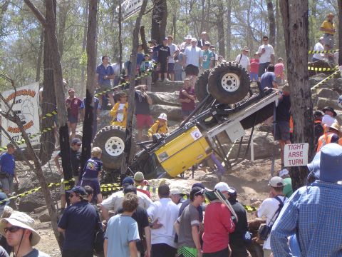 1982 Ford Bronco - An off-road event sees a yellow vehicle tipped onto its side, with a crowd gathered to observe the challenging course.