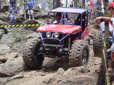1982 Ford Bronco - A custom-built off-road buggy navigates a rocky course with spectators watching.