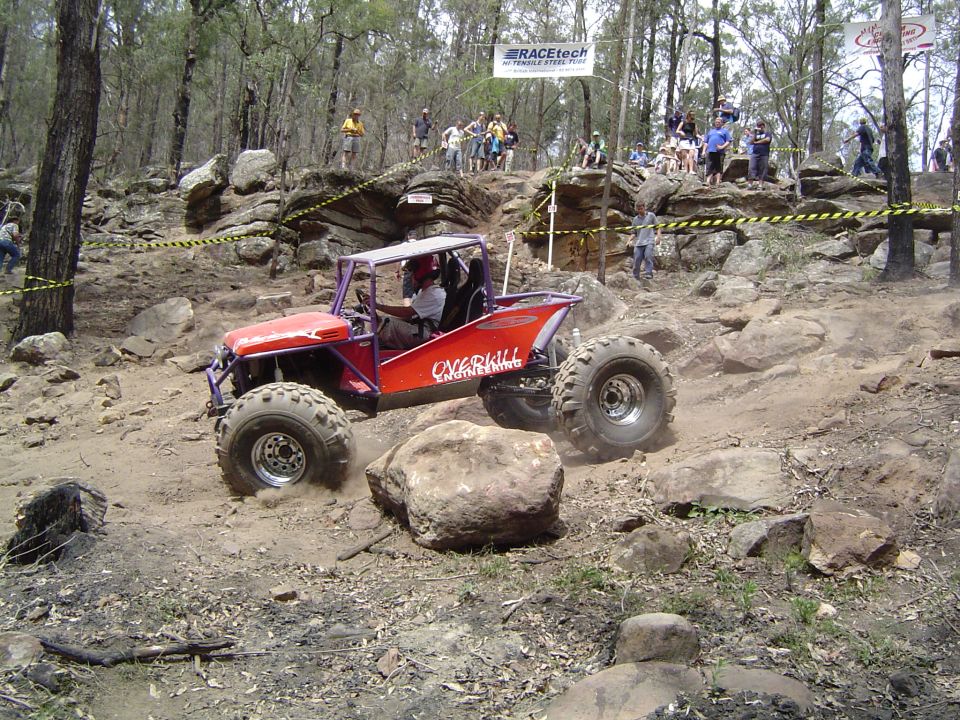 Red off-road buggy with purple roll cage and large tires navigates a rocky course