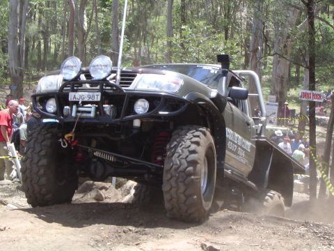 1982 Ford Bronco - An off-road vehicle navigates a challenging dirt course with spectators watching.