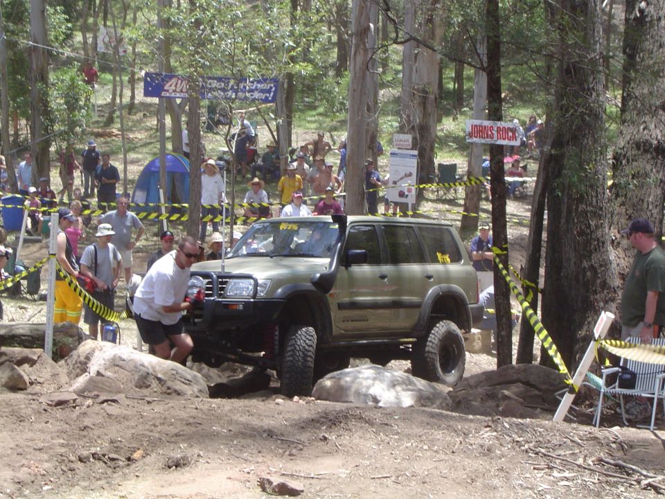 Off-road SUV with snorkel and bull bar maneuvering over rocks, spectators watch