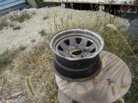 1992 Ford Bronco - A close-up of a dented wheel rim resting on a large wooden spool in a grassy area.
