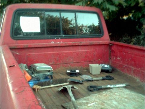 1978 Ford Bronco - The bed of a red pickup truck contains various tools, including shovels and a broom, ready for use.
