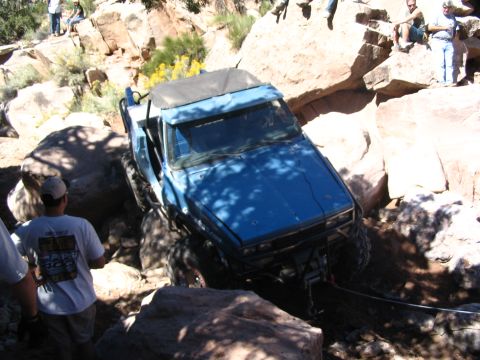 1988 Ford Bronco - A blue off-road vehicle is being winched through a difficult rocky terrain while onlookers observe.