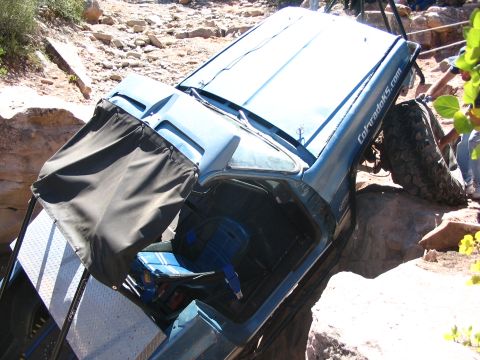 1988 Ford Bronco - A blue SUV is stuck in a rocky off-road obstacle, tilted precariously.