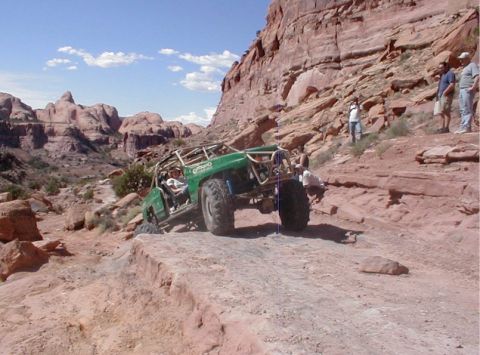 1988 Ford Bronco - A modified green off-road buggy navigates a challenging rocky terrain under a bright blue sky.