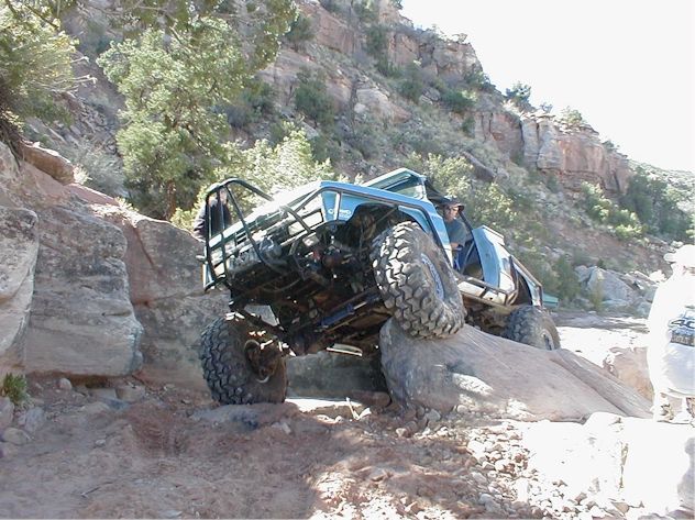 Off-road vehicle with roll cage climbing over a large rock on a trail