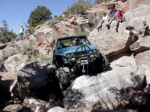 1988 Ford Bronco - A teal off-road truck is shown navigating a rocky terrain with people watching from above.