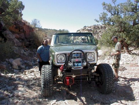 1988 Ford Bronco - A modified green SUV with oversized tires and a winch is parked on a rocky trail with two people standing nearby.