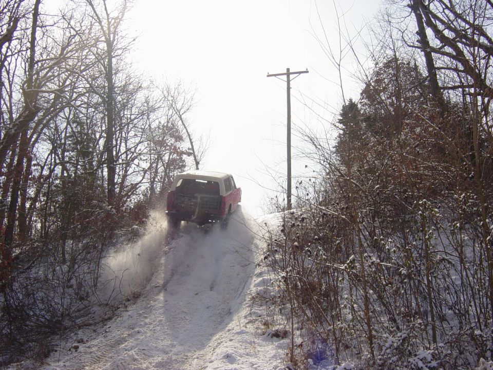 Red Ford Bronco with white top climbing a snowy trail, spraying snow from its tires