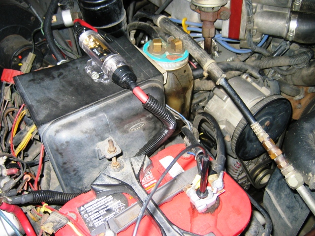 Engine bay with red battery, inline fuse holder, and red power cable in loom