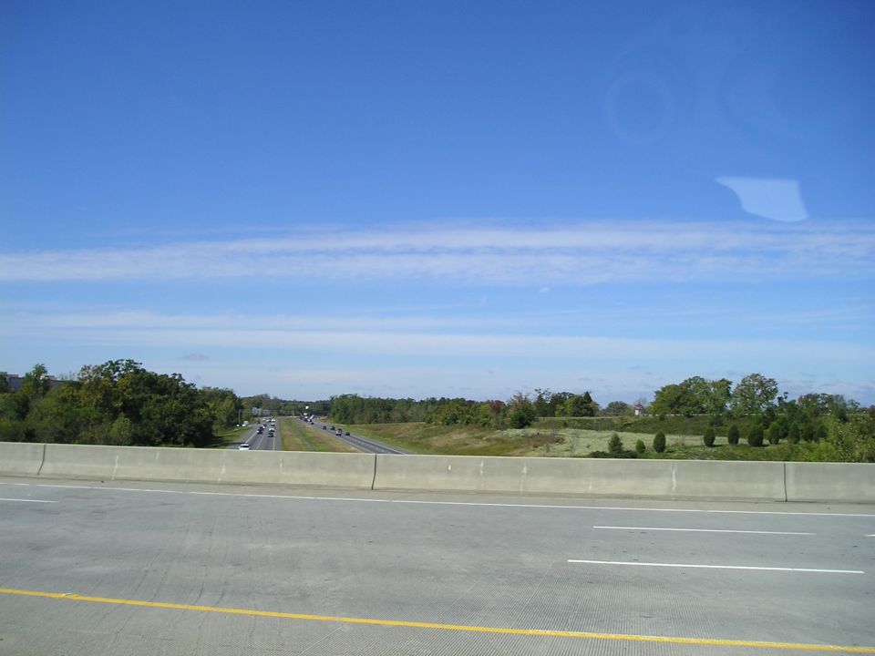 Highway overpass view of a divided highway with distant traffic, trees and blue sky