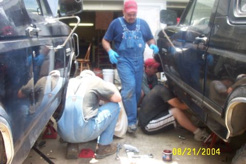 1979 Ford F-150 - Men work on the undercarriage of two dark pickup trucks in a garage setting.