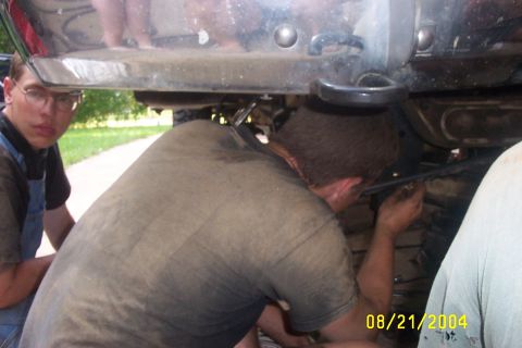 1979 Ford F-150 - Two individuals are seen working on the undercarriage of a vehicle, with a date stamp of 08/21/2004 visible.
