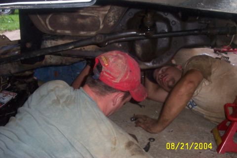 1979 Ford F-150 - Two men are working underneath a vehicle, with tools and parts scattered around.