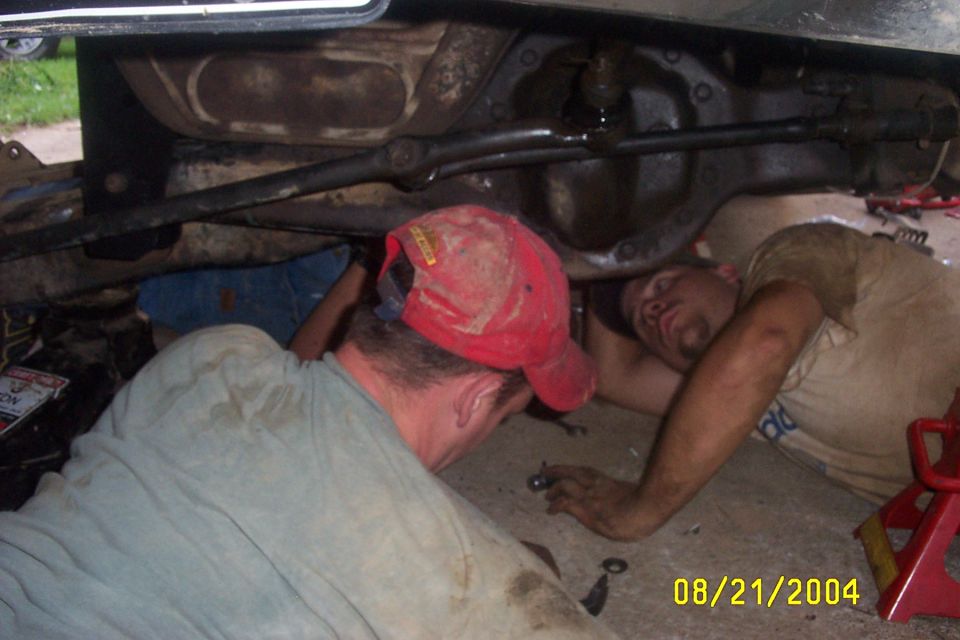 Underside of a vehicle with two mechanics working, one wearing a red cap