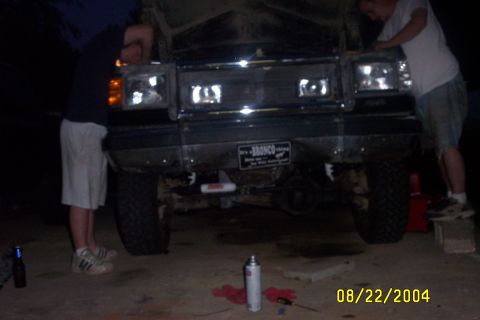 1979 Ford F-150 - Two people are working on the front end of a Ford Bronco, which has a license plate that reads "It's a BRONCO".