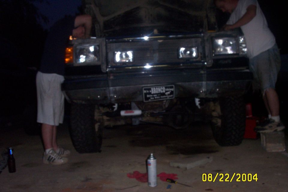 Two guys working on the front of a 1979 Ford Bronco. License plate says "It's a BRONCO"