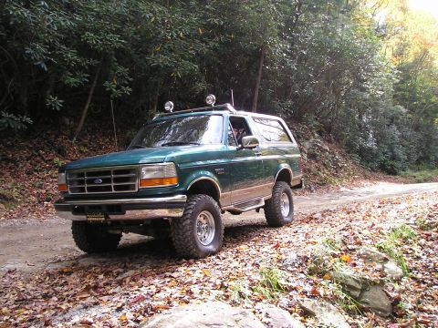 1996 Ford Bronco - A green Ford Bronco is seen on a dirt road surrounded by trees and fallen leaves.