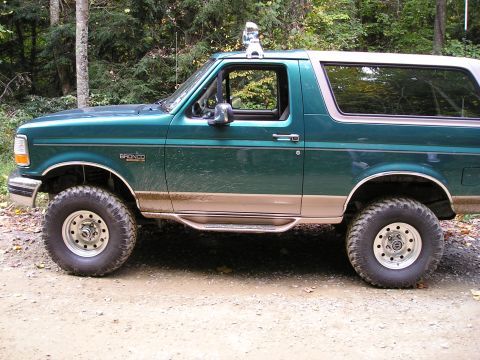 1996 Ford Bronco - This 1996 Ford Bronco is shown from the side, parked on a dirt road in a wooded area.