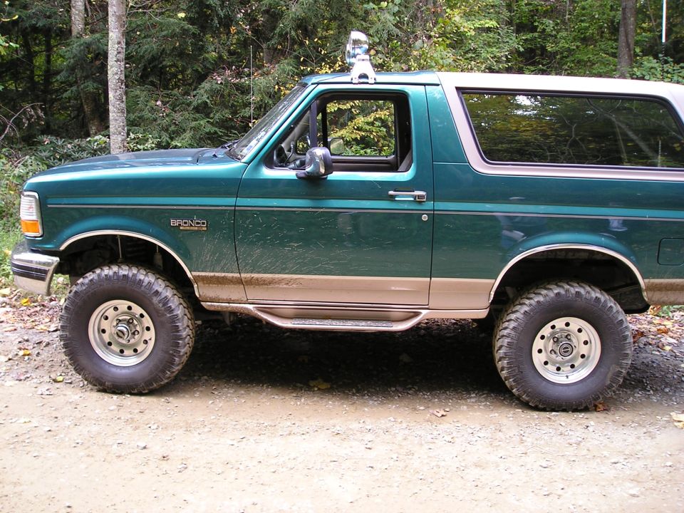 Green 1996 Ford Bronco parked on a dirt road with trees in the background