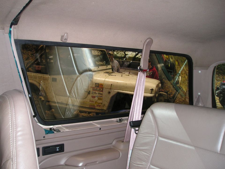View through a rear side window of a tan Jeep covered in stickers parked outdoors