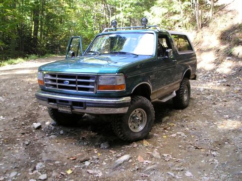 1996 Ford Bronco - Green 1996 Ford Bronco with roof rack and off-road tires sits on a rocky dirt path in a wooded area.