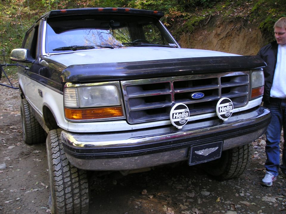Front of a lifted white and dark Ford pickup with chrome grille and twin Hella driving lights